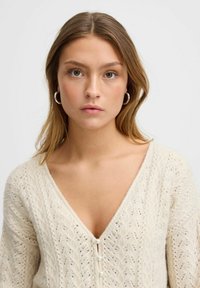 Krämfärgad stickad cardigan med V-hals som har ett strukturerat mönster och tre pärlemorknappar framtill.