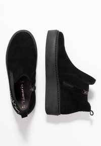 Černé semišové kotníkové boty s platformovou podrážkou, bočním zipem a dekoračními detaily vzadu. Hladký povrch a minimalistický design.