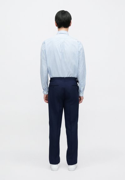 Camisa riscada azul e branca com gola abotoada, combinada com calças azul-marinho. As calças têm bolsos traseiros e um corte ajustado.