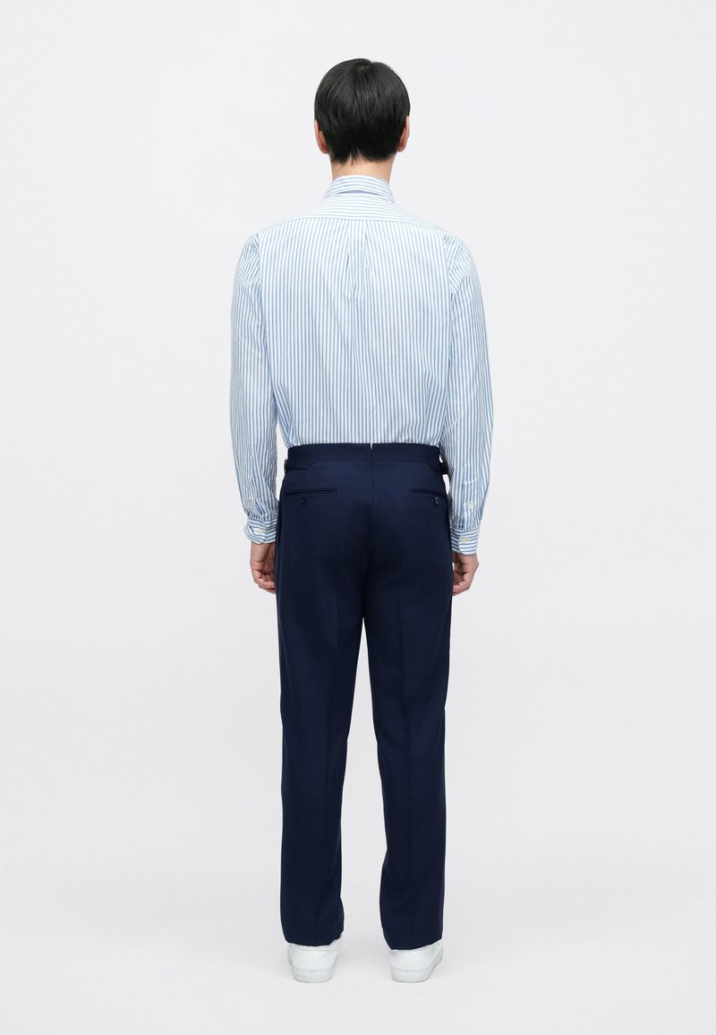 Striped blue and white dress shirt with button-down collar, paired with navy trousers. Trousers feature back pockets and a tailored fit.