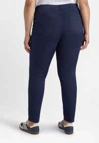 Donkerblauwe stretchbroek met een gladde textuur, voorzien van een elastische tailleband en twee achterzakken, gecombineerd met casual sneakers.