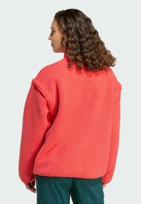 Coral fleece sweater met een hoge kraag, ontspannen pasvorm en verlaagde schouders; zachte textuur met naden langs de mouwen en het lichaam.