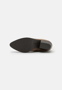 Zapato de ante marrón con punta afilada, parte superior texturizada y suela de goma negra con un patrón hexagonal y ligero tacón.