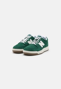 Green suede sneakers with white accents, featuring a perforated toe box, cushioned collar, and a rubber outsole. Classic lace-up design.