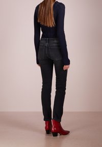 Marinblå ribbad långärmad topp i kombination med svarta figursydda jeans och röda ankelstövlar med en strukturerad klack och spetsig tå.