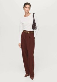 White long-sleeve top, brown belted high-waisted trousers, and pointed brown heels, holding a small dark bag. Simple design and tailored fit.