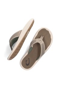 Beige teenslippers met geperforeerde banden, rubberen zolen en een bruine textuur voetbed. Heeft een logo op de band en groene accenten.