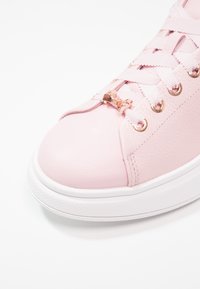 Baskets en cuir rose avec un bout arrondi, équipées de ferrures en or rose, de lacets en ruban, et d'une semelle en caoutchouc blanche. Détail de panneau latéral texturé.