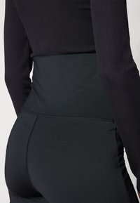 High-waisted black leggings with a smooth, stretchy fabric, featuring stitched seams and a sleek design for a fitted appearance.