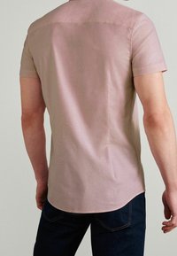 Korte mouwen shirt van zachte, lichtroze stof met een gladde textuur. Beschikt over een eenvoudig ontwerp en subtiele stiksels op de schouders.