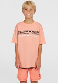 T-shirt rosa chiaro con un logo grafico in bianco e nero sul petto, abbinata a pantaloni da bagno arancioni con logo sulla cintura nera.