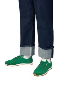 Sneakers verdi in suede e mesh con suola bianca. Indossati con jeans in denim scuro con risvolto che mostra un tessuto più chiaro.