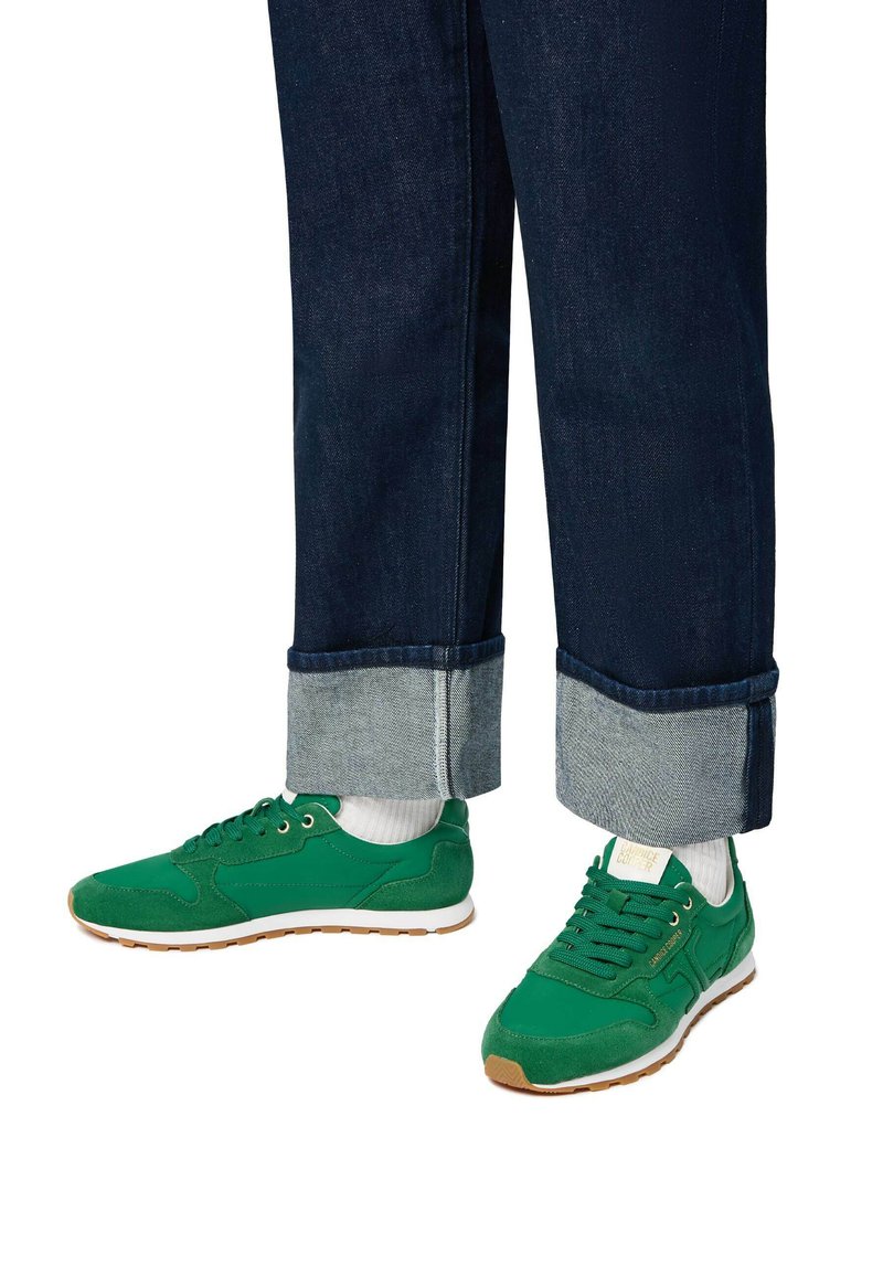 Sneakers verdi in suede e mesh con suola bianca. Indossati con jeans in denim scuro con risvolto che mostra un tessuto più chiaro.