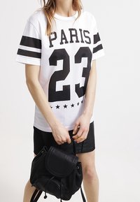 Vit nättröja med svart text "PARIS" och nummer "23," med svarta randaccenter. Matchad med en svart ryggsäck.