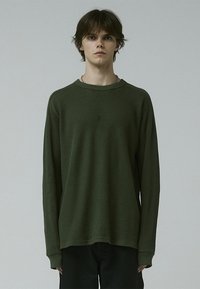 Long-sleeve, olive green thermal shirt with a textured knit fabric. Features a round neckline and dropped shoulders, offering a relaxed fit.