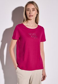T-shirt fuchsia à manches courtes avec un col rond et des manches retroussées, ornée d'un texte brodé argenté "NE JAMAIS DOUTER de soi" sur le devant.