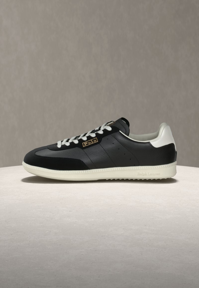 Melns ādas sneakeris ar baltām detaļām, teksturētu virsu, apaļu purngala daļu, metāla logotipu un gumijas zolīti. Klasisks dizains ar mežģīņu aizdari.