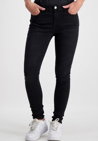 Zwarte skinny jeans, gemaakt van denim, met een hoge tailleband en vijf zakken. Het model draagt witte sneakers. Soepele textuur en geen zichtbare patronen.