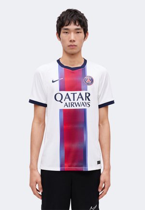 Mladý muž stojaci, oblečený v bielom futbalovom drese Paris Saint-Germain s červeným a modrým vertikálnym pásom a logom Qatar Airways.