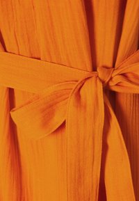 Tissu orange avec une apparence texturée et légère, présentant une ceinture nouée à la taille et des détails de couture visibles.
