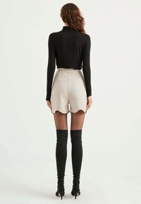 Zwarte langemouwen top gecombineerd met hoog-taille, beige scalloped shorts. Model draagt kniehoge zwarte laarzen. Glad materiaal, gestroomlijnd ontwerp.