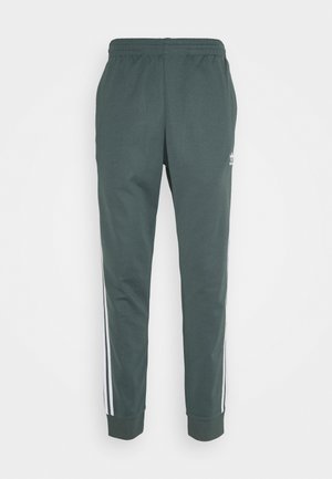 Pantalon de sport vert foncé avec taille élastique, jambes fuselées, bandes blanches sur les côtés et petit logo sur la partie supérieure de la cuisse.