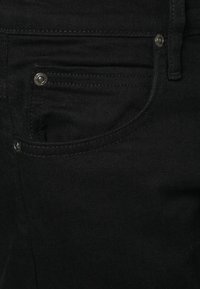 Svarta denimjeans med en framficka med en nitar, stickade detaljer och en slät textur. Materialet verkar slitstarkt och enhetligt.