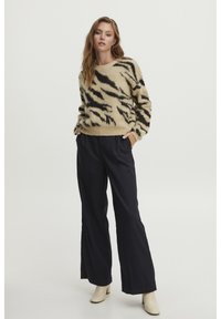 Beige, pluizig sweater met zwarte tijgerstrepen, gecombineerd met donkere, wijde broekspijpen en crèmekleurige enkellaarsjes. Zachte textuur, ontspannen pasvorm.