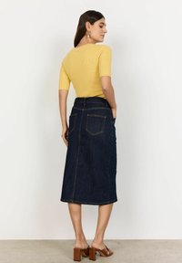 Denim midi kjol med mörkblå tvätt, rak passform, bakfickor och synliga söm detaljer. Matchas med en gul ribbad topp och bruna klacksandaler.