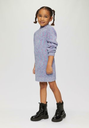 Lila gestricktes Kleid mit strukturiertem Finish, überschnittenen Schultern und umgeschlagenen Ärmeln, kombiniert mit schwarzen Schnürstiefeletten.