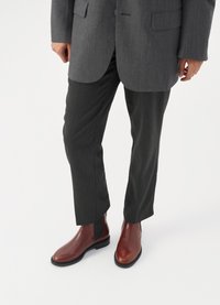 Pantalons ajustés gris foncé avec des fines rayures, associés à des bottes de cheville en cuir marron avec des panneaux élastiques sur les côtés et un design élégant.