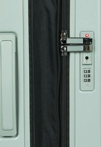 Hartschalenkoffer in mattem Grün mit einem schwarzen Reißverschluss, Kombinationsschloss und TSA-zugelassener Sicherheitsvorrichtung. Glatte, strapazierfähige Oberflächenstruktur.