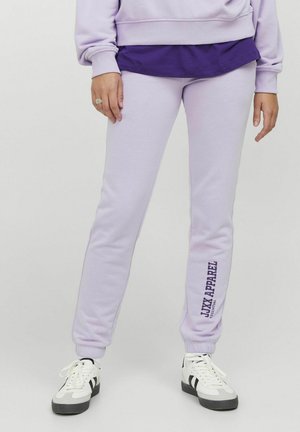 Pantalones jogger en color lila, confeccionados en tela suave, con un diseño ajustado, puños acanalados y estampado de logo en el lateral. Combinados con zapatillas blancas.