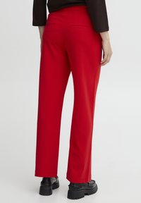 Red trousers with a straight leg design, featuring back pockets and a smooth fabric texture. Paired with black platform shoes.