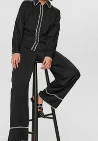 Chemise noire à manches longues et pantalon large avec des coutures contrastantes blanches. Le pantalon a un ourlet évasé, associé à des ballerines noires pointues.