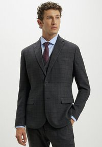 Giacca da abito a quadri grigia con rever a punta, due tasche frontali e chiusura a un bottone. Abbinata a una camicia azzurro chiaro e una cravatta bordeaux.