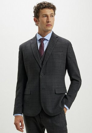Giacca da abito a quadri grigia con rever a punta, due tasche frontali e chiusura a un bottone. Abbinata a una camicia azzurro chiaro e una cravatta bordeaux.