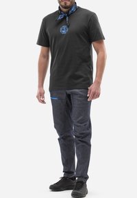 Czarna koszulka z krótkim rękawem z niebieskim logo, zestawiona z ciemnoniebieskimi dżinsami z niebieską kieszonką akcentującą. Uzupełniona czarnymi tenisówkami.