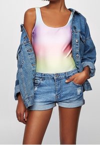 Costume da bagno con una sfumatura di colori pastello (rosa, viola e verde) abbinato a un giubbotto in denim azzurro chiaro e pantaloni corti in denim strappati.