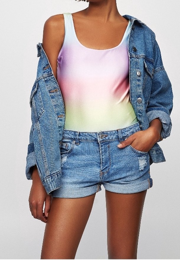 Costume da bagno con una sfumatura di colori pastello (rosa, viola e verde) abbinato a un giubbotto in denim azzurro chiaro e pantaloni corti in denim strappati.