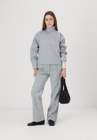 Grå oversized genser med høy hals, kombinert med grå vid bukser og en svart flettet håndveske. Glatt tekstur, avslappet passform.