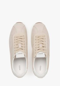 Beżowe zamszowe sneakersy z zaokrąglonym noskiem, materiałowymi sznurówkami, białą gumową podeszwą i wytłoczonym logo na języku. Minimalistyczny design z tonalnym przeszyciem.