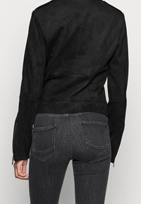 Svart mockajacka med en figursydd design, som har en jämn yta, synliga sömmar och en lätt böjd nederkant.