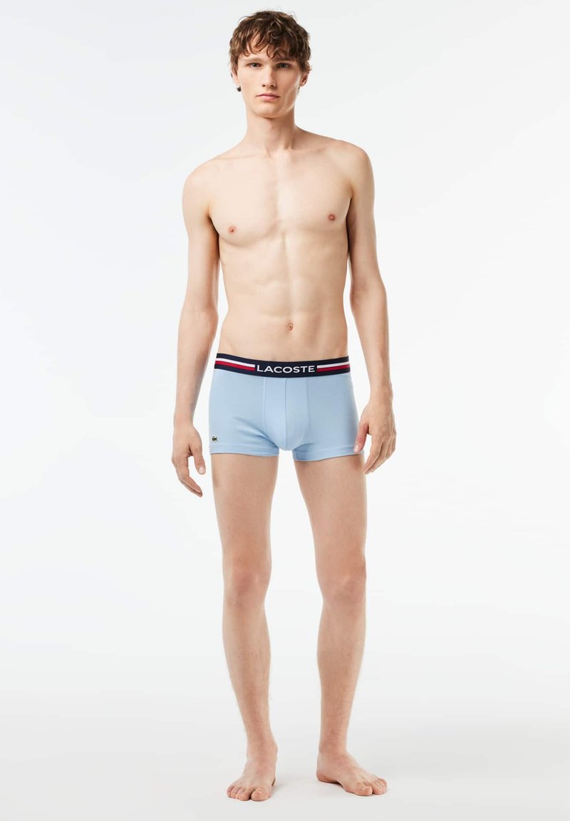 Boxers pour hommes bleu clair avec une ceinture à rayures noire et rouge. Comprend un petit logo vert sur l'ourlet gauche. Texture du tissu douce.