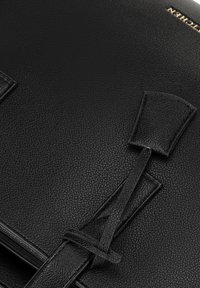Schwarze Lederhandtasche mit strukturiertem Oberflächenmaterial, geometrischen Ausschnitten und einem gebundenen Lederriemendetail zum Verschluss.