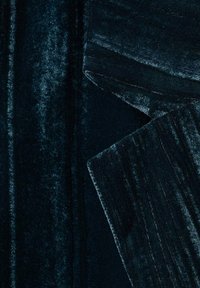 Material de catifea verde închis cu o textură moale și pufoasă. Are linii verticale și margini pliate, ceea ce îi sporește profunzimea și detaliile.