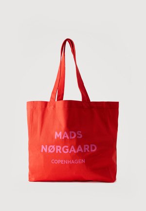 Sarkanas auduma somiņa ar divām rokturiem un rozā tekstu "MADS NØRGAARD COPENHAGEN" priekšpusē uz baltas fona.