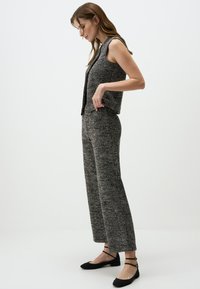 Graues, gestricktes ärmelloses Top und dazu passende weite Hose mit strukturiertem Muster und lässiger Passform. Schwarze Ballerinas mit Knöchelriemen.