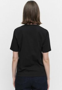 Svart bomullströja med korta ärmar och rund hals, med en slät textur och inga synliga tryck eller mönster, sedd bakifrån.