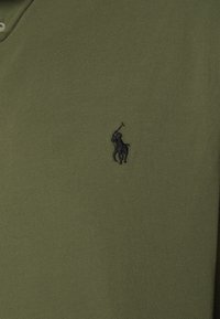 Oliwkowa koszulka polo wykonana z teksturowanej tkaniny, z małym wyszywanym czarnym logo konia i jeźdźca na lewej piersi.